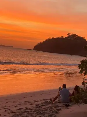 a couple sitting on the beach watching the sunset at Bonito apartamento 103 frente a la piscina 100mt del mar in Playa Flamingo
