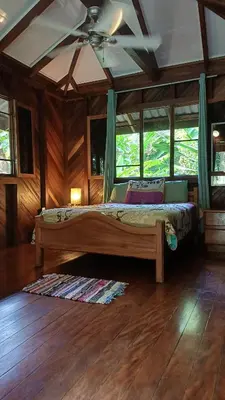 a bedroom with a bed with a ceiling fan at Wooden Cabin with deck Over Creek, walk to beach in Dominicalito
