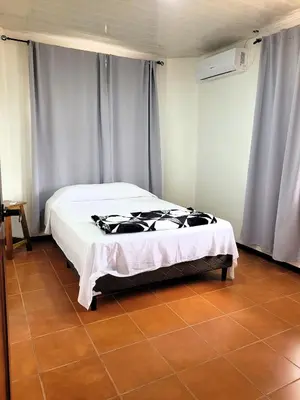 a bedroom with a bed with white sheets and blue curtains at Arenal Mountain Apartments in Fortuna