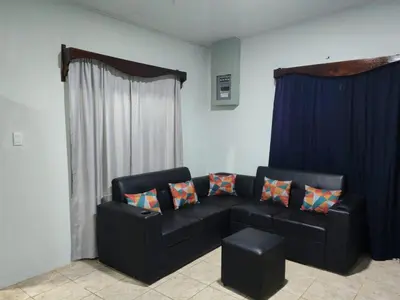 a living room with a black couch and blue curtains at Nayon Vacation Home in Portegolpe