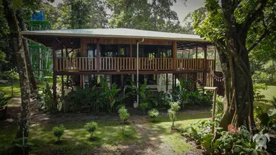 a wooden house with a deck in a garden at Casa Shec- An Oceanfront Jungle Retreat in Drake