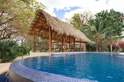 a large swimming pool with a thatch roof and a resort at Playa Flamingo Ocean View Retreat in Playa Flamingo