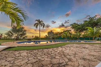 a pool in a park with palm trees and a sunset at Casa Colinas Pickleball in Playa Grande