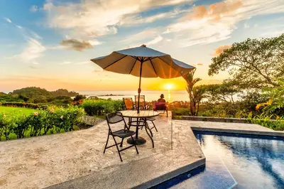 a table with an umbrella and chairs next to a pool at Ocean-Mountain views 2 Bdr, Villa Pelicano in Dominicalito