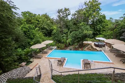 a swimming pool with patio furniture and umbrellas at Tulemar Resort in Manuel Antonio