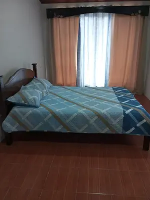 a bed with a blue comforter and a window at Ordoñez in Bijagua
