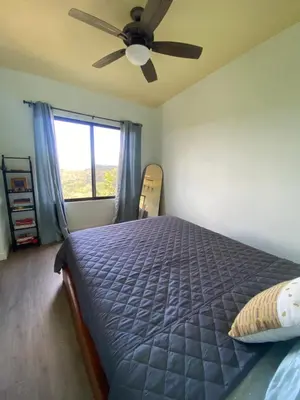a bedroom with a bed with a ceiling fan and a window at Hawk Hope Tiny House with Sunset Views in Bagaces
