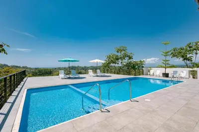a swimming pool with chairs and umbrellas at Hospedaje Quepos Tardes Doradas in Quepos