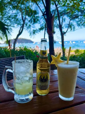 a bottle of beer and two drinks on a wooden table at Calm & Palms Second Floor Studio in Coco