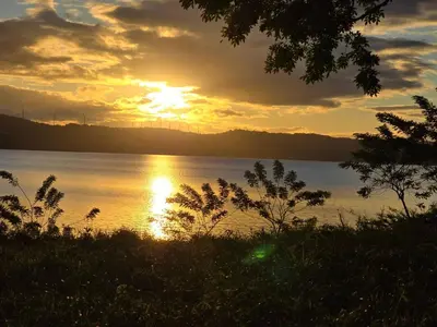 a sunset over a body of water with trees at SeStudio Lodge in Nuevo Arenal with Jungle Views in Nuevo Arenal