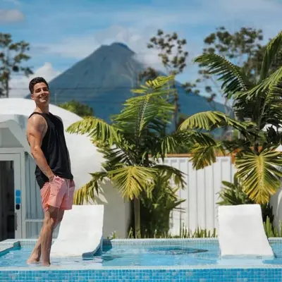 a man standing in a swimming pool with a mountain in the background at Arenal Igloo Private House in Fortuna