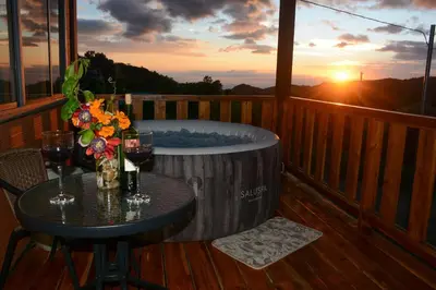a hot tub on a deck with a table and wine glasses at Cabaña Los Lirios in Monteverde Costa Rica