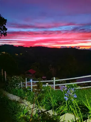 a sunset in the mountains with a white fence and flowers at Cerro Lodge & Gardens in Cartago