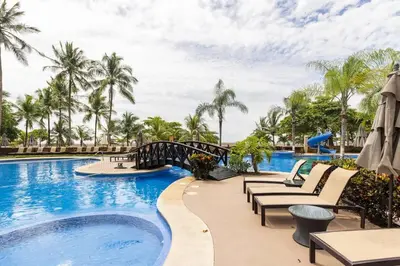 a pool at a resort with chairs and a bridge at 2 Bedroom Condo in Croc's Casino Resort in Jacó