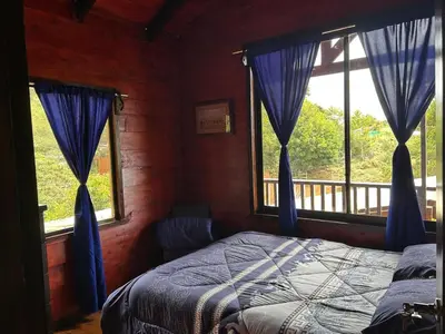 a bedroom with blue curtains and a bed and windows at Cabaña de Montaña El Jardin in Jardín