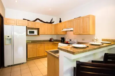 a kitchen with wooden cabinets and a white refrigerator at Beautiful Condo in Peaceful Cliffside Location with a Private Balcony & Stunning Ocean and Mountain Views in Playa Flamingo