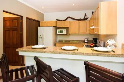 a kitchen with a counter with two chairs and a refrigerator at Beautiful Condo in Peaceful Cliffside Location with a Private Balcony & Stunning Ocean and Mountain Views in Playa Flamingo