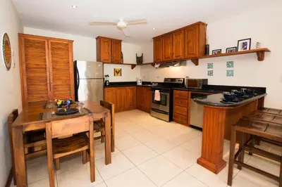 a kitchen with wooden cabinets and a table and a refrigerator at Cozy Garden Condo with Vibrant Tropical Decor, Swimming Pool and Rancho in Brasilito