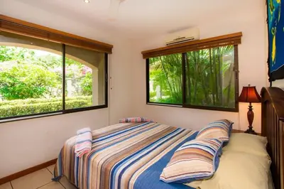 a bedroom with a bed and two windows at Cozy Garden Condo with Vibrant Tropical Decor, Swimming Pool and Rancho in Brasilito