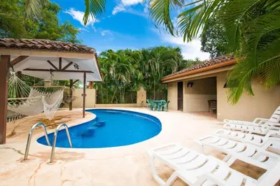 a pool with chairs and a hammock next to a house at Cozy Garden Condo with Vibrant Tropical Decor, Swimming Pool and Rancho in Brasilito