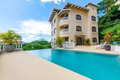 a house with a swimming pool in front of it at Top-Floor Condo with Sweeping Ocean, Mountain & Marina Views in Playa Flamingo