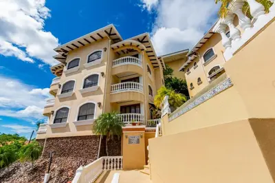 a large yellow building with palm trees in front of it at Top-Floor Condo with Sweeping Ocean, Mountain & Marina Views in Playa Flamingo