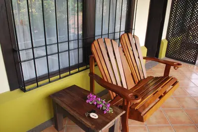 a rocking chair and a table with flowers on a porch at Dos Palmas Studio Apartments in Alajuela City