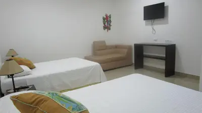 a room with two beds and a chair and a television at Sueño Tranquilo in Quepos