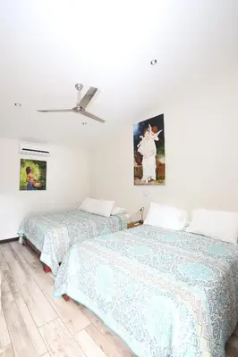 two beds in a white room with paintings on the wall at Casa María Aeropuerto B&B in Alajuela City