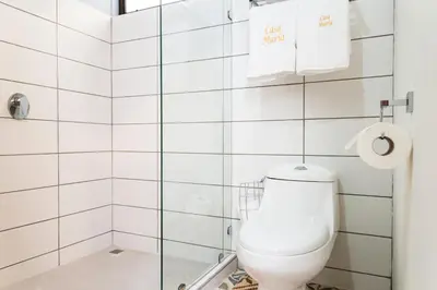 a bathroom with a toilet in a white tiled wall at Casa María Aeropuerto B&B in Alajuela City