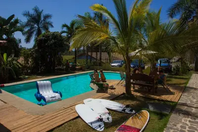 a group of people sitting around a swimming pool with surfboards at Wipeout Guest House in Jacó