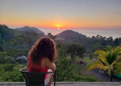 a woman sitting in a chair watching the sunset at Pura Natura Lodge Manuel Antonio in Manuel Antonio