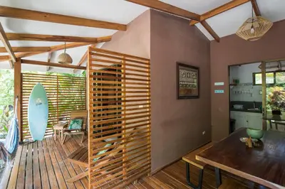 a room with a table and a surfboard on a deck at Ohana Villas in Santa Teresa Beach