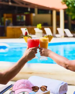 two people holding up drinks at a table near a pool at Aninga Lodge in Tortuguero