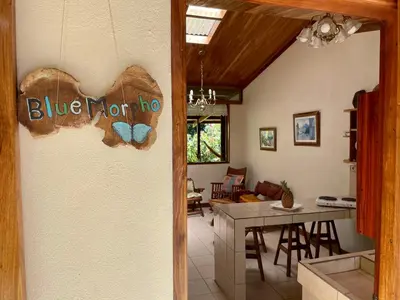 a living room with a blue butterfly sign on the wall at Finca Isla Rainforest Retreat in Aguas Zarcas
