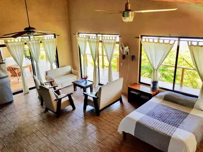 a bedroom with a bed and two chairs and windows at Santa Teresa Surf Vista Villas in Santa Teresa Beach
