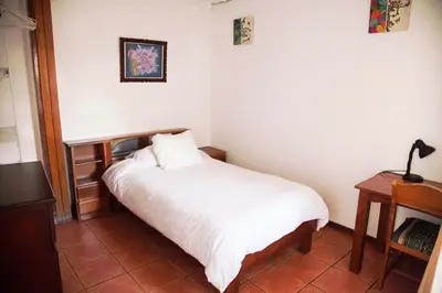 a small bedroom with a white bed and a desk at Casa Kibi Kibi in San José