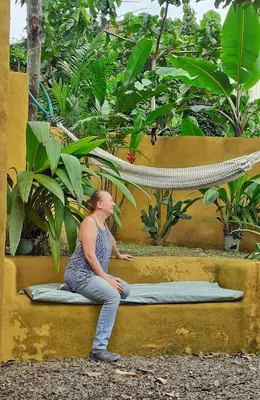 a woman sitting on a bench in front of plants at Montaña Linda Guest House Orosi in Orosí