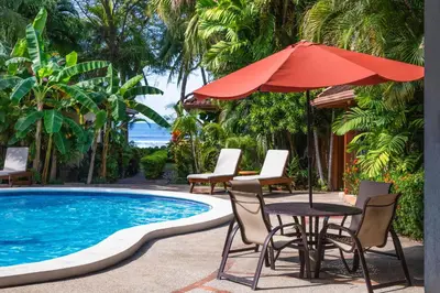a table with an umbrella next to a swimming pool at The Coast Beachfront Hotel in Tamarindo