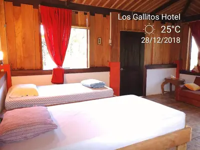 two beds in a room with a red curtain at Los Gallitos Eco Lodge in San Miguel
