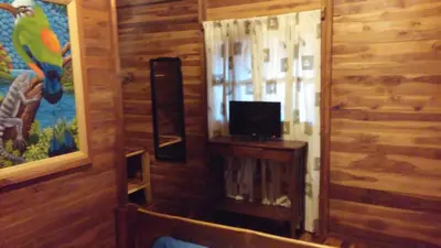 a room with a television and a window in a wooden wall at Hotel Cabañas La Teca in Liberia