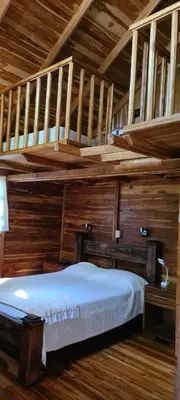 a bed in a room with wooden walls and stairs at Congos Hostal y Camping in Playa Hermosa