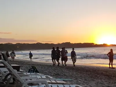 a group of people walking on the beach at sunset at Hotel La Palapa in Tamarindo