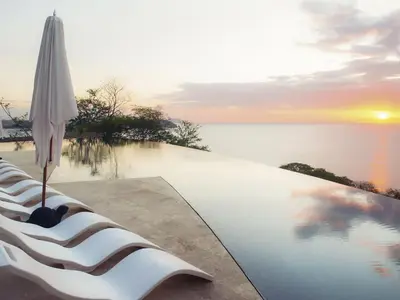 a pool with an umbrella and chairs next to the water at Casa Chameleon Hotel Las Catalinas - Adults Only in Playa Flamingo