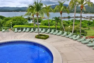 a swimming pool with chairs and a view of the water at Oceanview Studio Apartment with Community Pool & Views of Flamingo Marina in Playa Flamingo