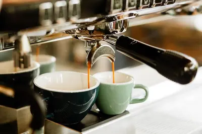 a coffee machine pouring coffee into two coffee cups at Paradise Hot Springs - Thermal Water & Volcano Views in Fortuna