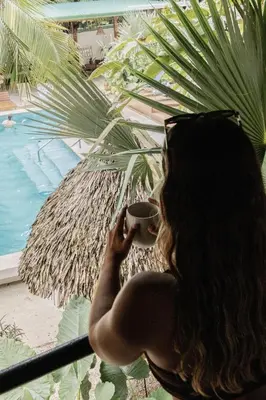 a woman holding a cup of coffee in front of a palm tree at ESO Santa Teresa in Santa Teresa Beach