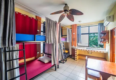 a room with bunk beds and a table and a ceiling fan at Sandy Toes Hostel in Sámara