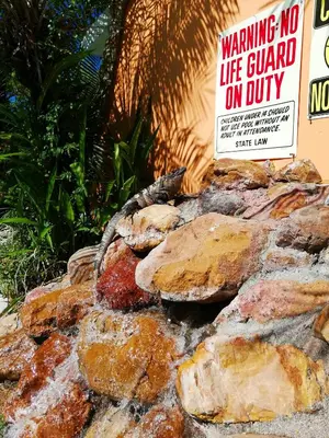 a sign that reads warning no lifeguard on duty on rocks at Villas Verdes in Sámara