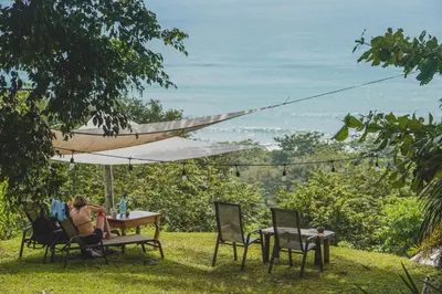 a woman sitting at a table under an umbrella at Hotel Buenos Aires in Santa Teresa Beach